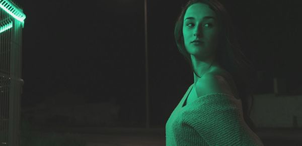 Green light on young woman looking away against sky at night