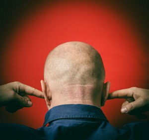 Rear view of mature man with fingers in ears against red background