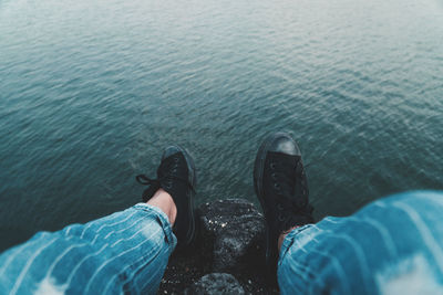 Low section of man sitting on rock at sea