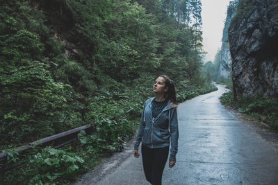 Woman looking up while standing on road in forest