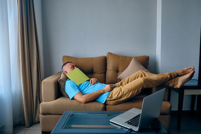 Young adult caucasian man felt asleep on a couch dropped book on face. tired man sleeps on sofa