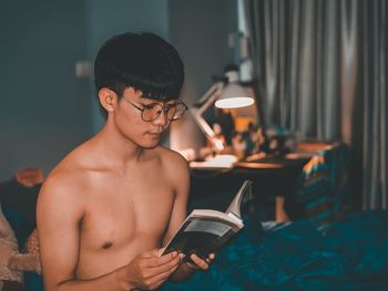 Shirtless man reading book at home