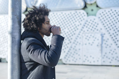 Side view of young man standing against wall