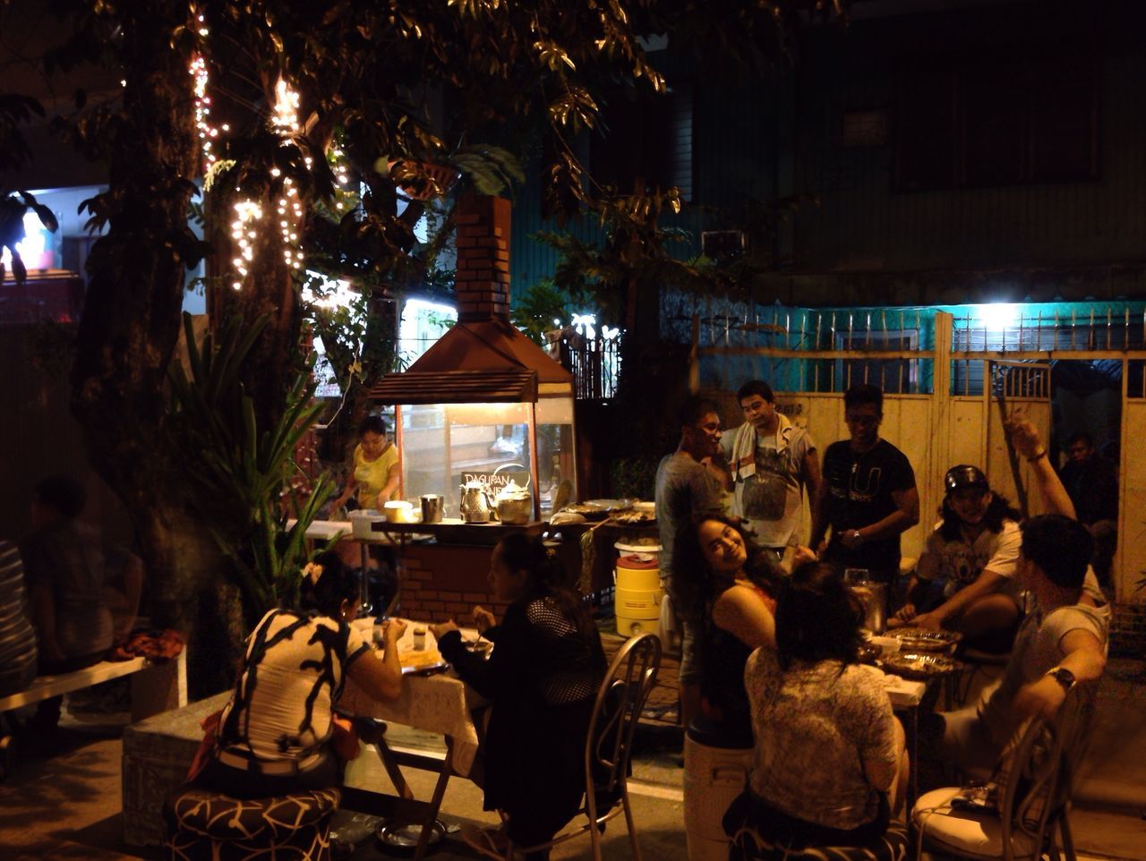 chair, men, table, sitting, lifestyles, tree, person, restaurant, night, leisure activity, large group of people, illuminated, built structure, building exterior, architecture, sidewalk cafe, market, food and drink, relaxation