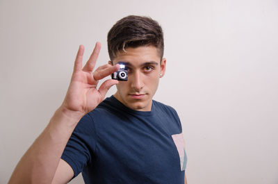 Portrait of young man holding eyeglasses against white background