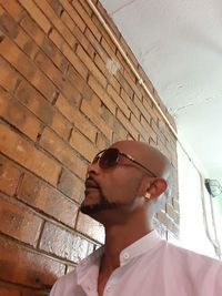 Low angle view of young man wearing sunglasses standing against wall