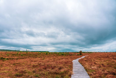 Dirt road passing through field against sky