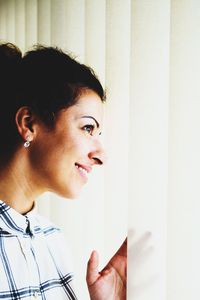 Happy young woman looking through blinds