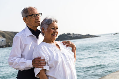 Senior couple standing at beach against clear sky