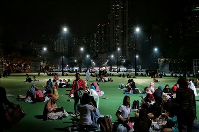 People relaxing in park against buildings at night in city