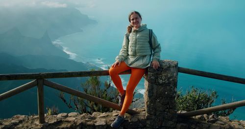 Young woman standing on railing against mountains in tenerife, anaga.