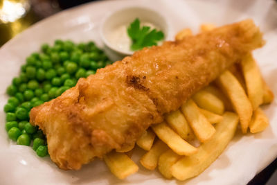 Close-up of fried fish with french fries and peas served in plate