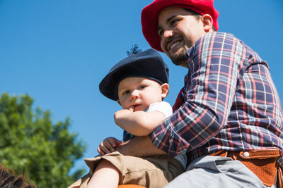 Father holding baby boy against sky