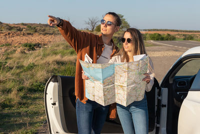 Young beautiful couple holding a map with a car behind them trying to look for the way back home.