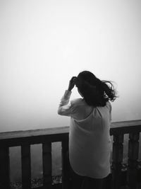 Rear view of woman standing by railing against foggy weather