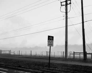 Road sign by electricity pylon against sky