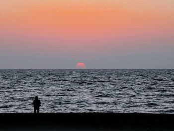 Silhouette man standing on beach against clear sky during sunset