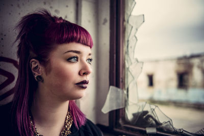 Close-up of thoughtful young woman by broken window in building