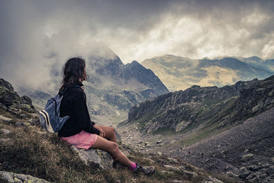 Side view of woman sitting on mountain against cloudy sky