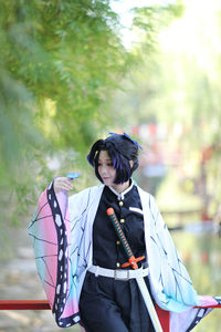 Woman holding umbrella while standing against trees