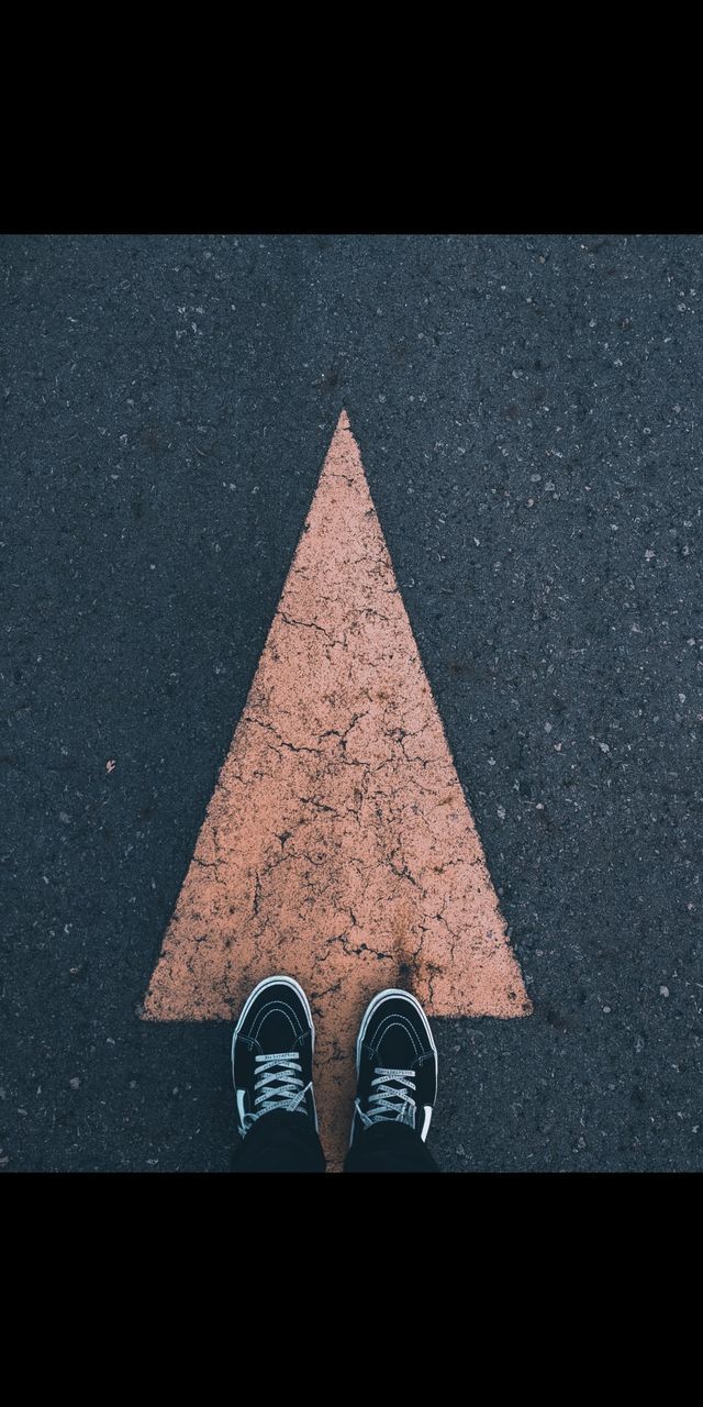 low section, human leg, shoe, one person, road, personal perspective, high angle view, standing, shape, street, triangle, circle, city, geometric shape, blue, sign, transportation, black, triangle shape, outdoors, asphalt, directly above, day, symbol