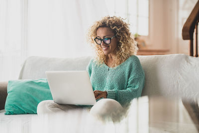 Smiling woman using laptop while sitting on sofa at home