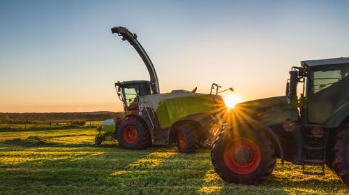 Tractors on agricultural field against sky during sunset