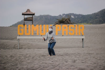 Portrait of woman wearing pollution mask while standing against alphabet at sandy beach