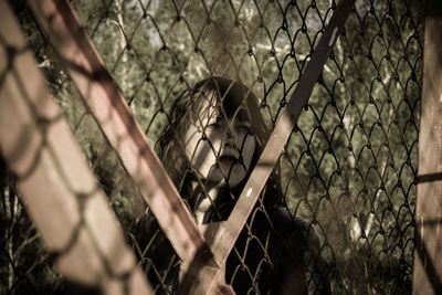 Thoughtful woman looking through chainlink fence