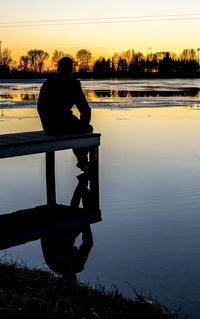 Rear view of silhouette man looking at lake against sky