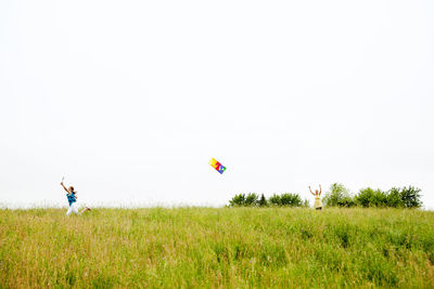 Girl running with kite on grassy field against clear sky