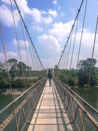 Rear view of man walking on footbridge against sky