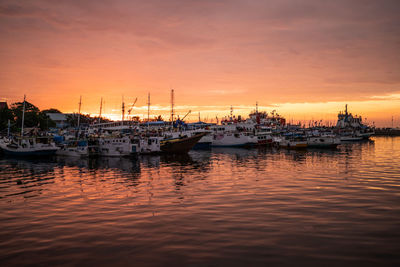 Sailboats moored in harbor during sunset