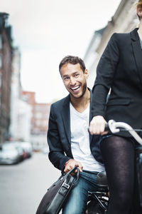 Portrait of happy businessman enjoying bicycle ride with colleague on street