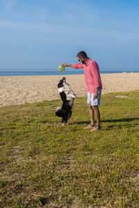 Bearded man playing with dog at beach in sunny day