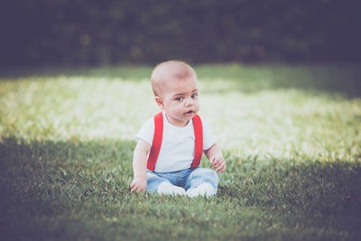 Portrait of cute boy sitting on grassy field