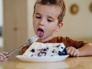 Pretty caucasian boy eating a cake with a fork at home