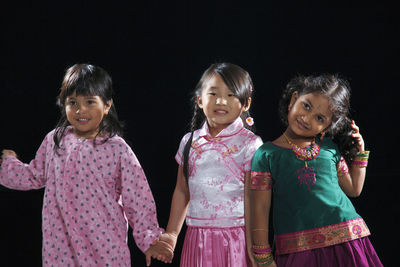 Portrait of smiling girls standing against black background