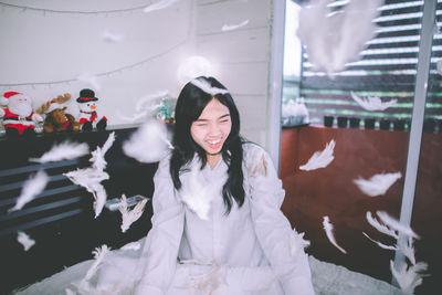 Cheerful young woman playing with feathers in bedroom at home