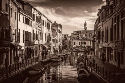 Boats moored in canal amidst buildings against sky