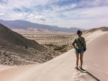 Full length of woman standing on sand dune against sky