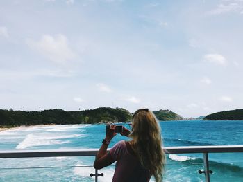 Rear view of woman photographing sea against sky