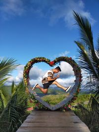 Young woman by palm trees against blue sky