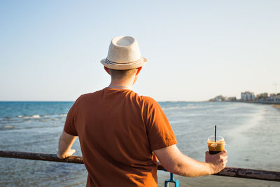 Rear view of man standing by sea against sky