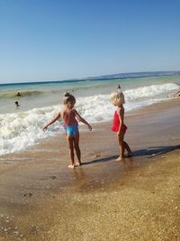 Girls playing at shore against clear sky