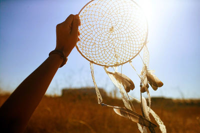 Cropped hand of person holding dream catcher at sunset