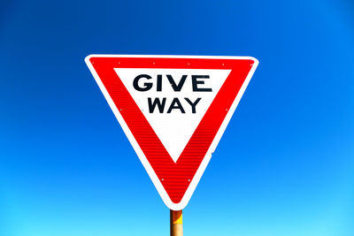 Low angle view of road sign against blue sky