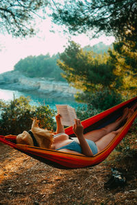 Woman lying down on hammock by trees