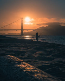 Silhouette man fishing in sea against sky during sunset