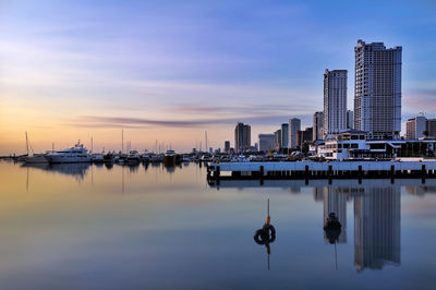 Sailboats in city by buildings against sky during sunset